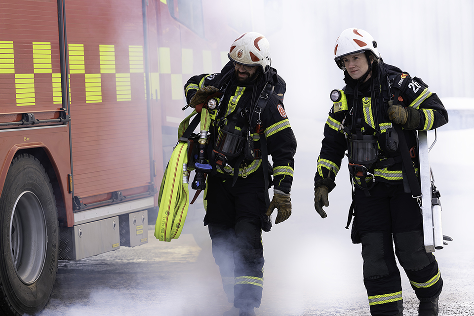 En kvinna och en man i larmställ som går bredvid en brandbil