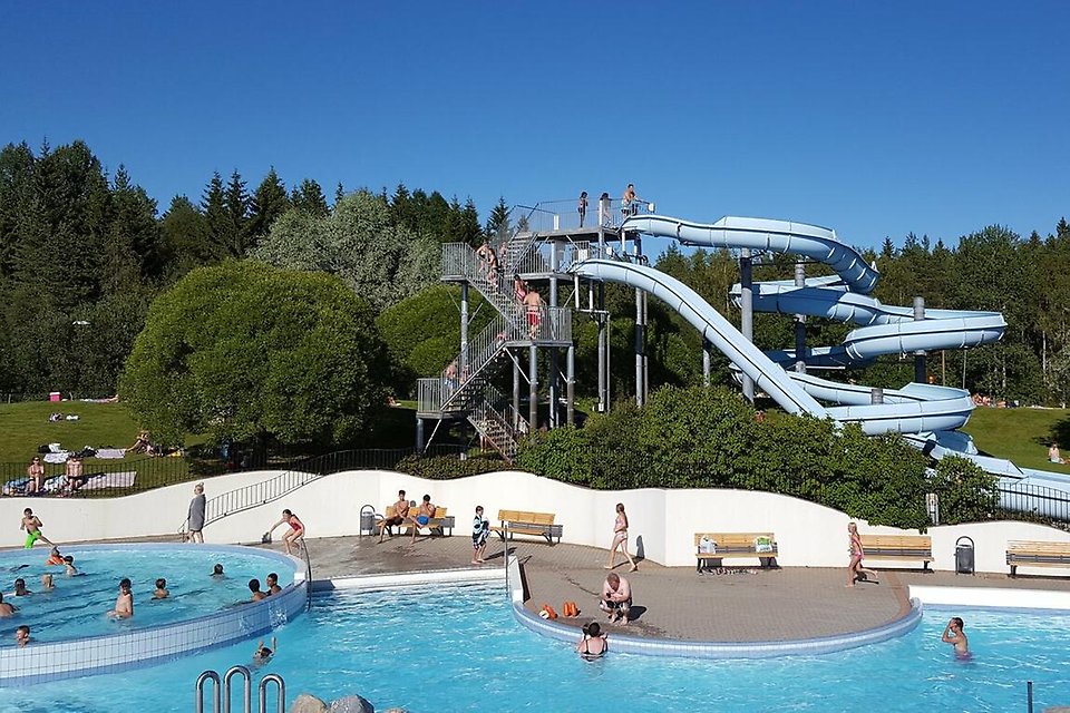 Pojke med simglasögon sitter och ler på bassängkanten.