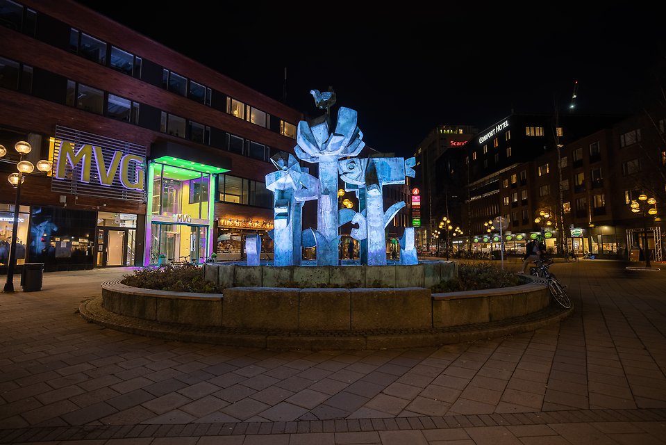 Kvällsbild på Renmarkstorget där Stig Lindbergs staty är upplyst.